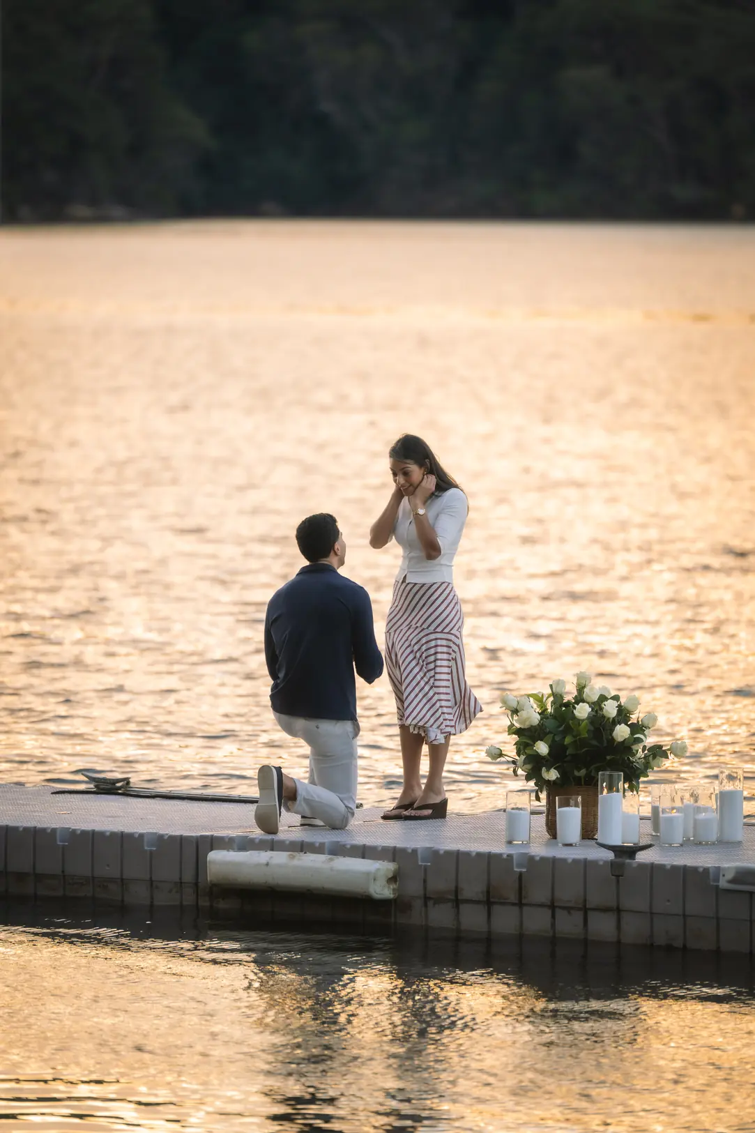 Man kneeling to propose on a candle-lit jetty at golden hour