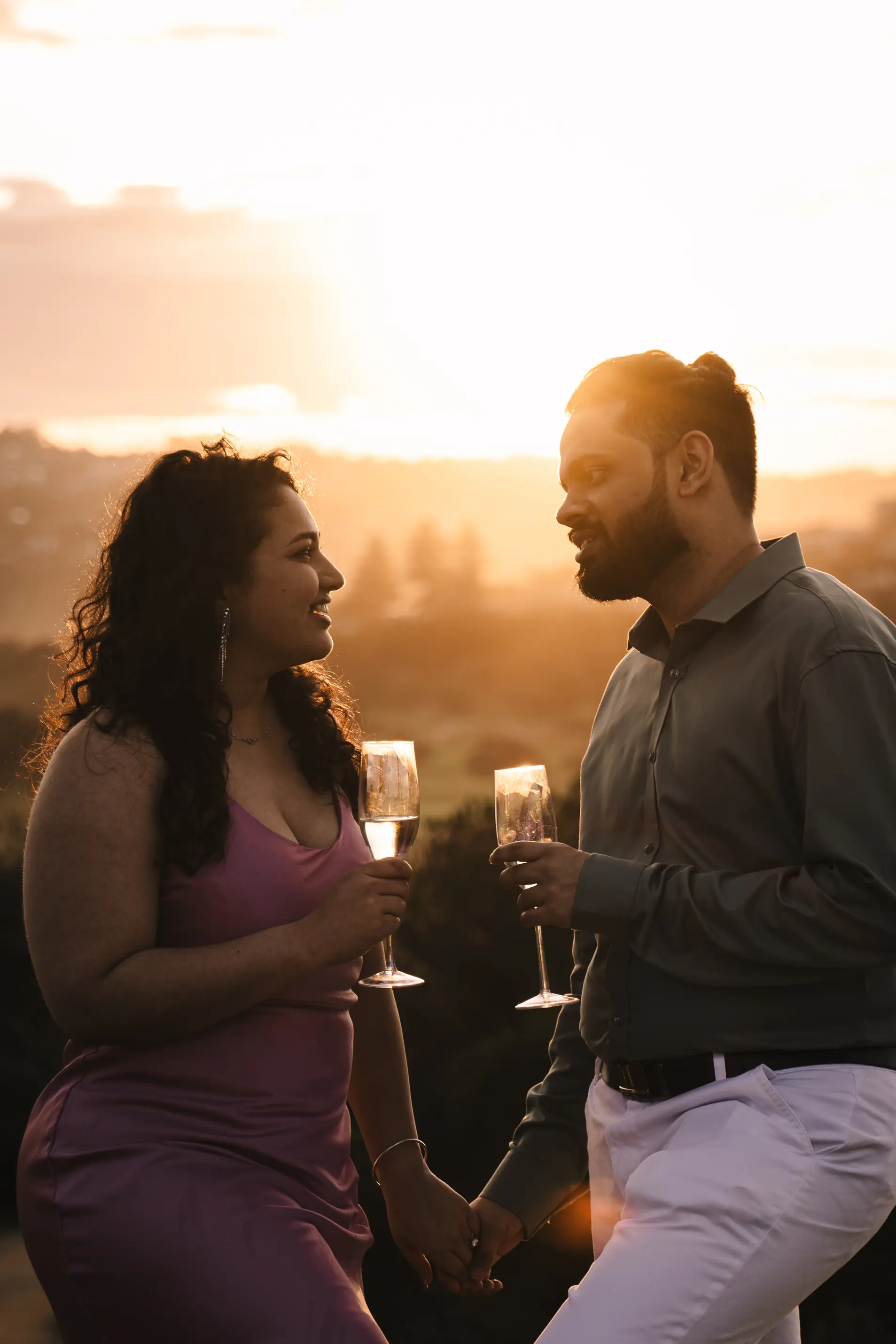 Newly engaged couple clinking champagne glasses at golden hour on a Sydney headland