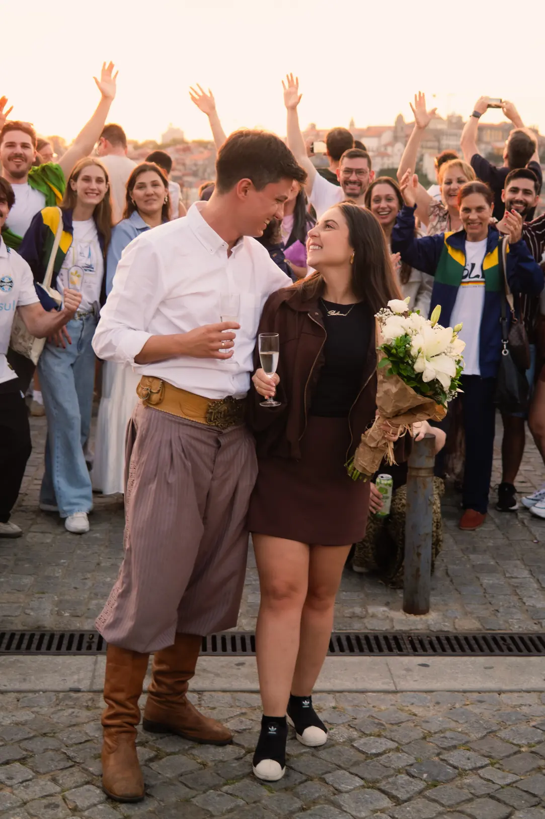A newly engaged couple with champagne and flowers as a crowd cheers behind them in Porto, Portugal