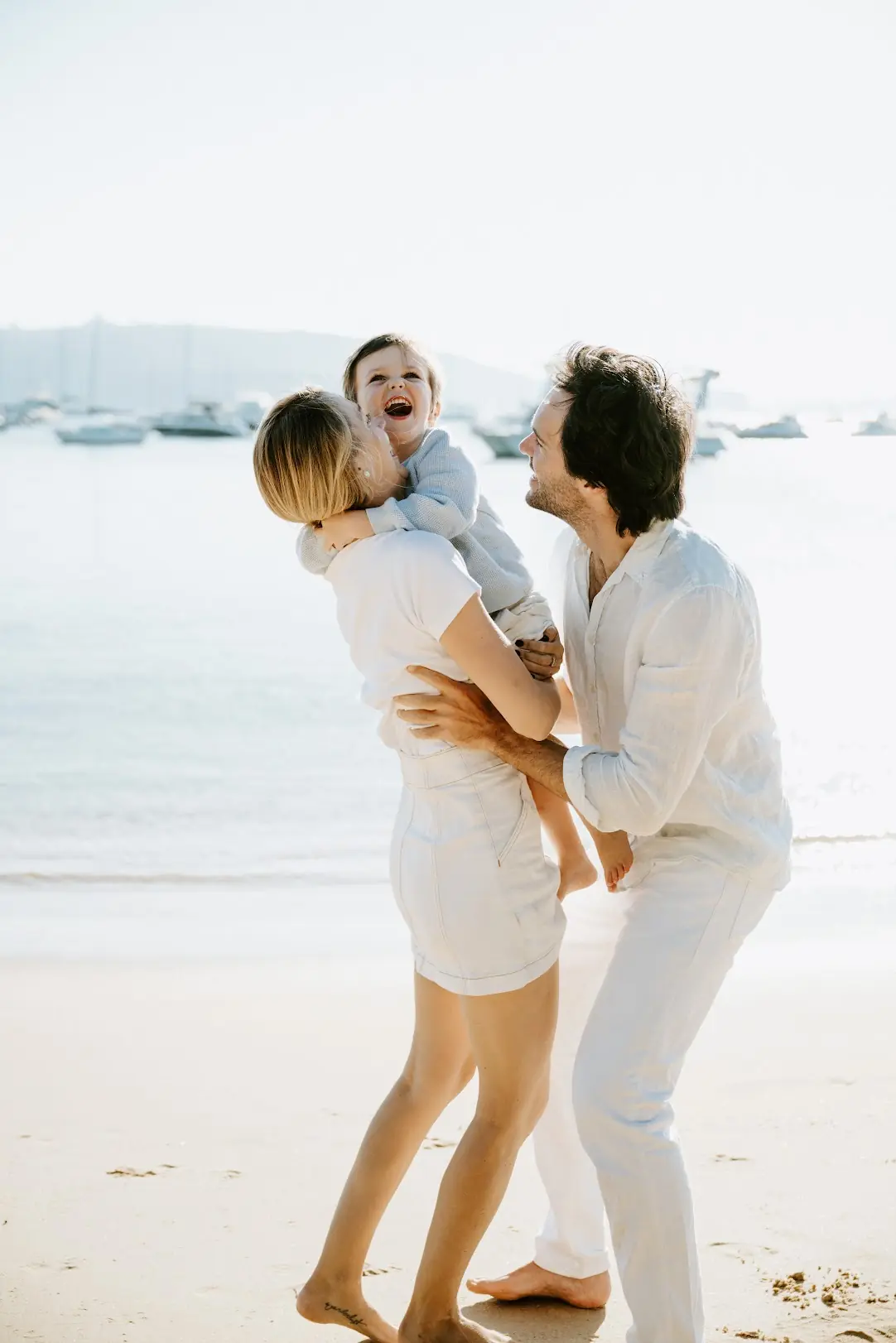 Parents laughing with their toddler on a calm Sydney harbour beach