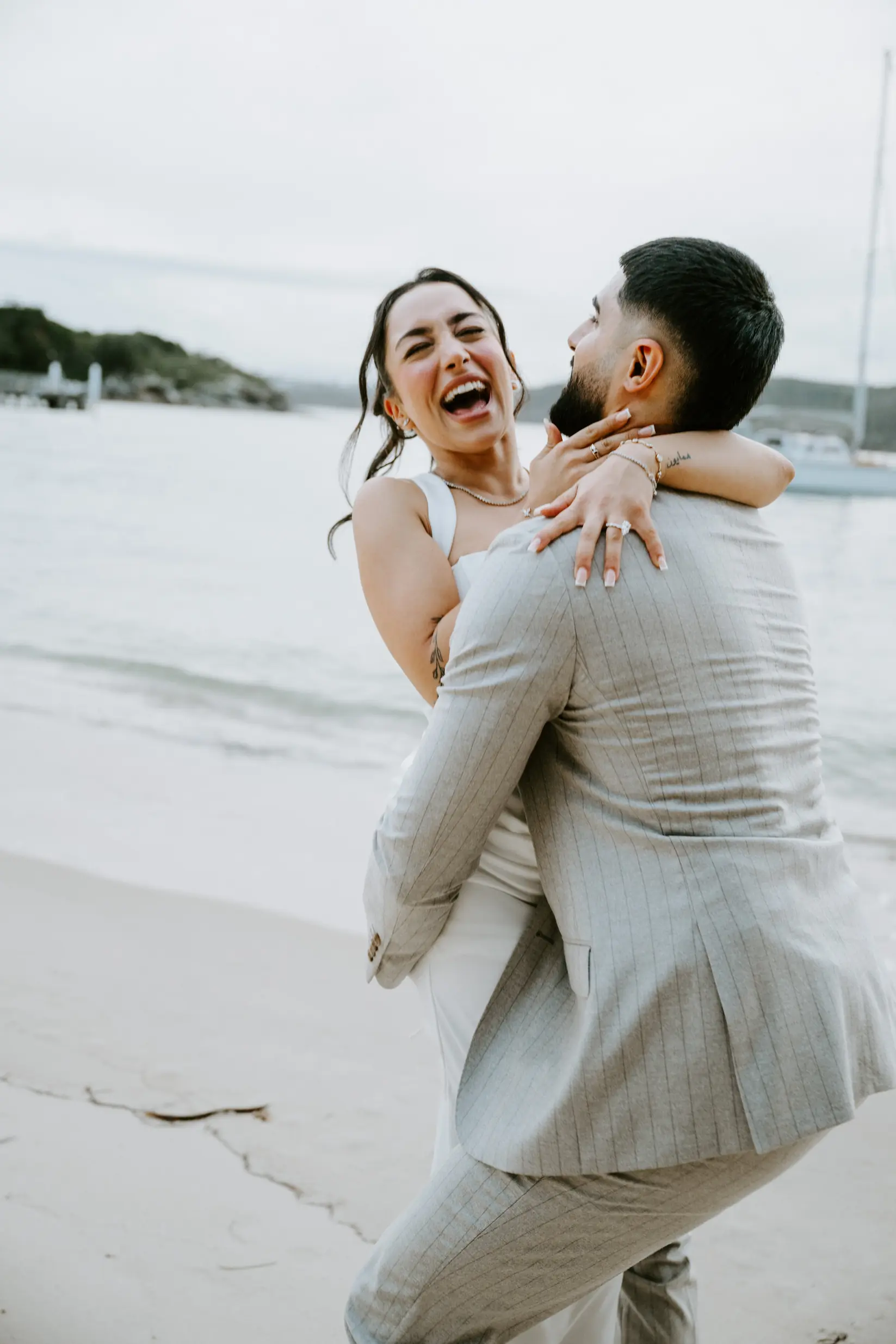 Groom carrying his new fianc&eacute;e on the beach, laughing, just after she said yes